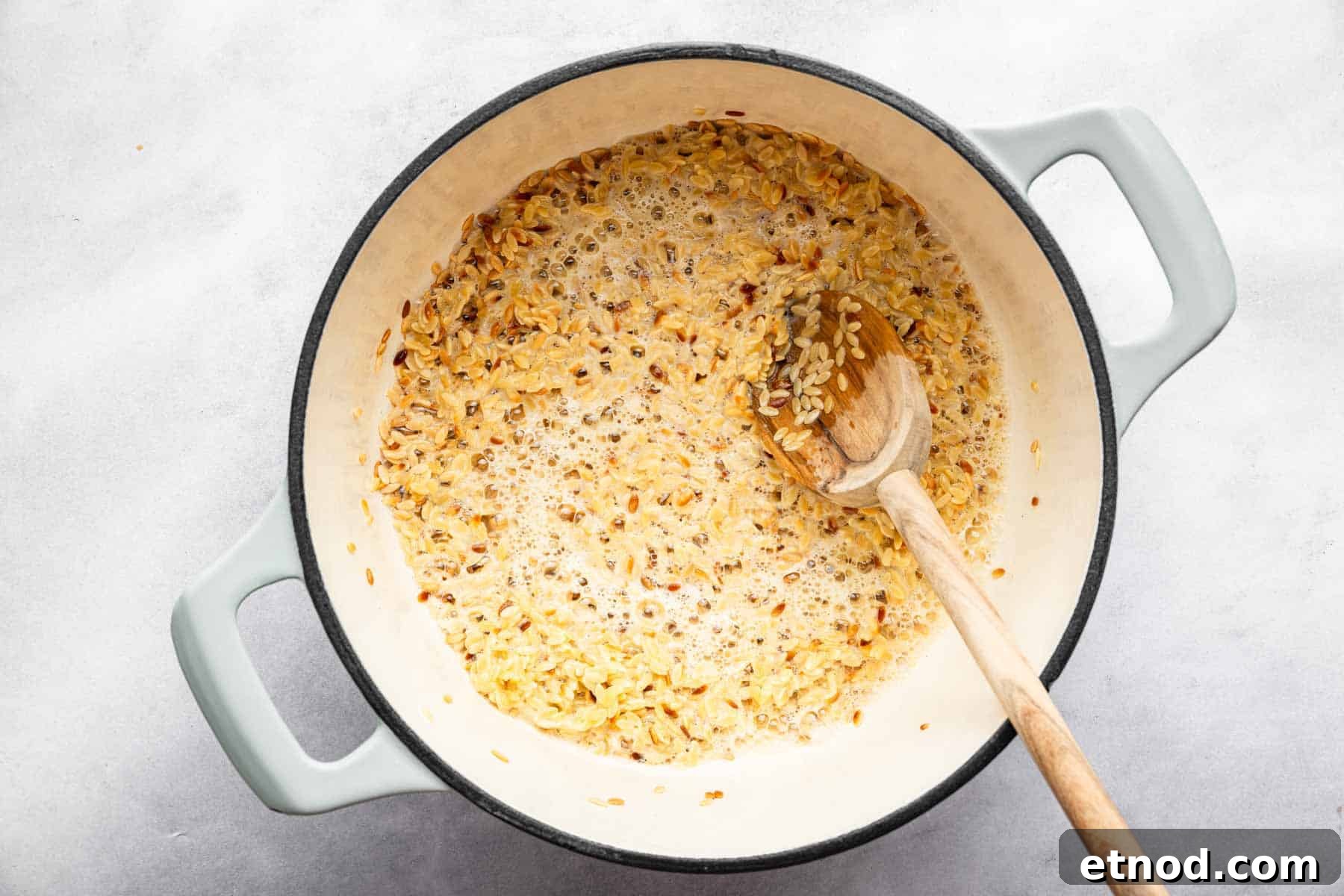 Creamy Lemon Orzo with Parmesan and Fresh Herbs 4 White dutch oven with pasta sizzling and wooden spoon.
