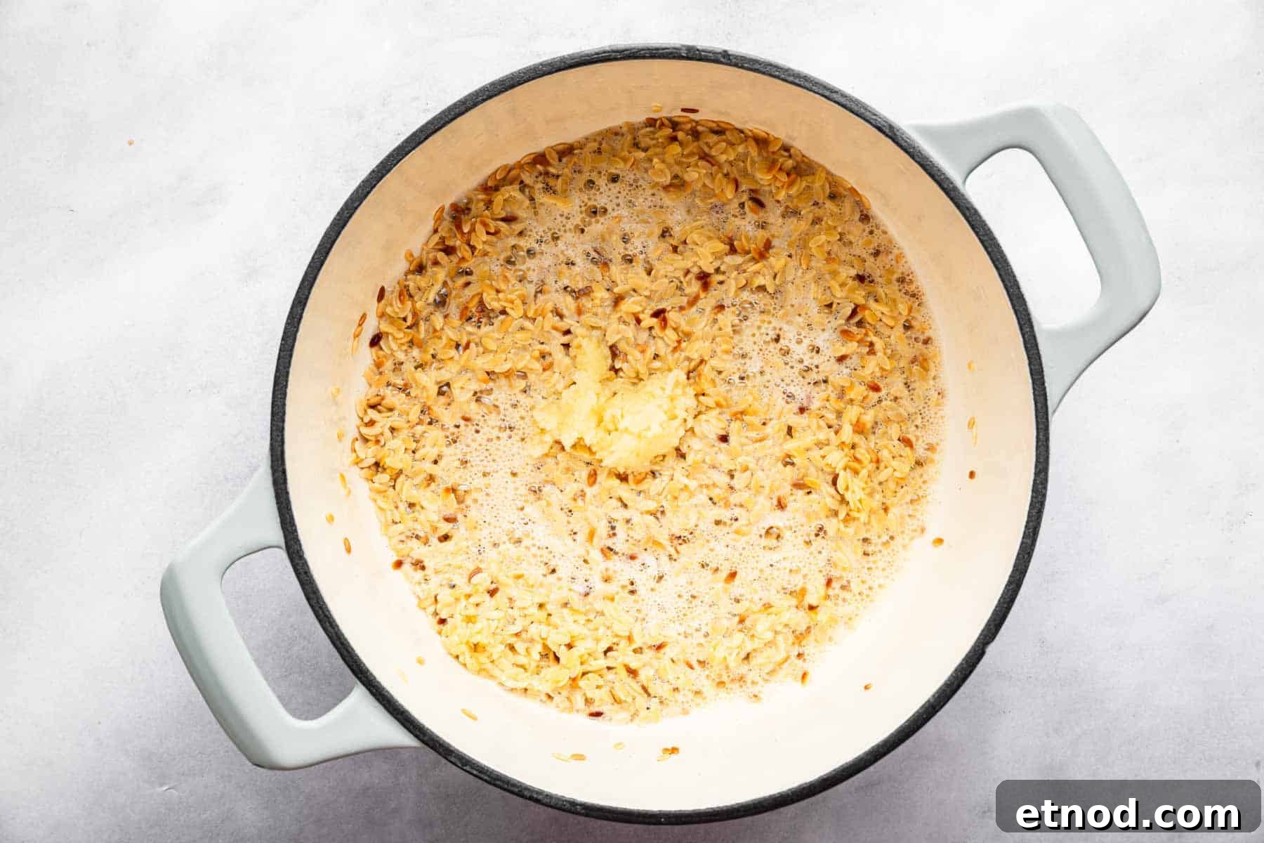 Creamy Lemon Orzo with Parmesan and Fresh Herbs 5 Minced garlic in a pan with sizzling pasta.