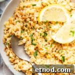 Creamy Lemon Orzo with Parmesan and Fresh Herbs 9 Bowl of lemon orzo garnished with lemon slices and a spoon.