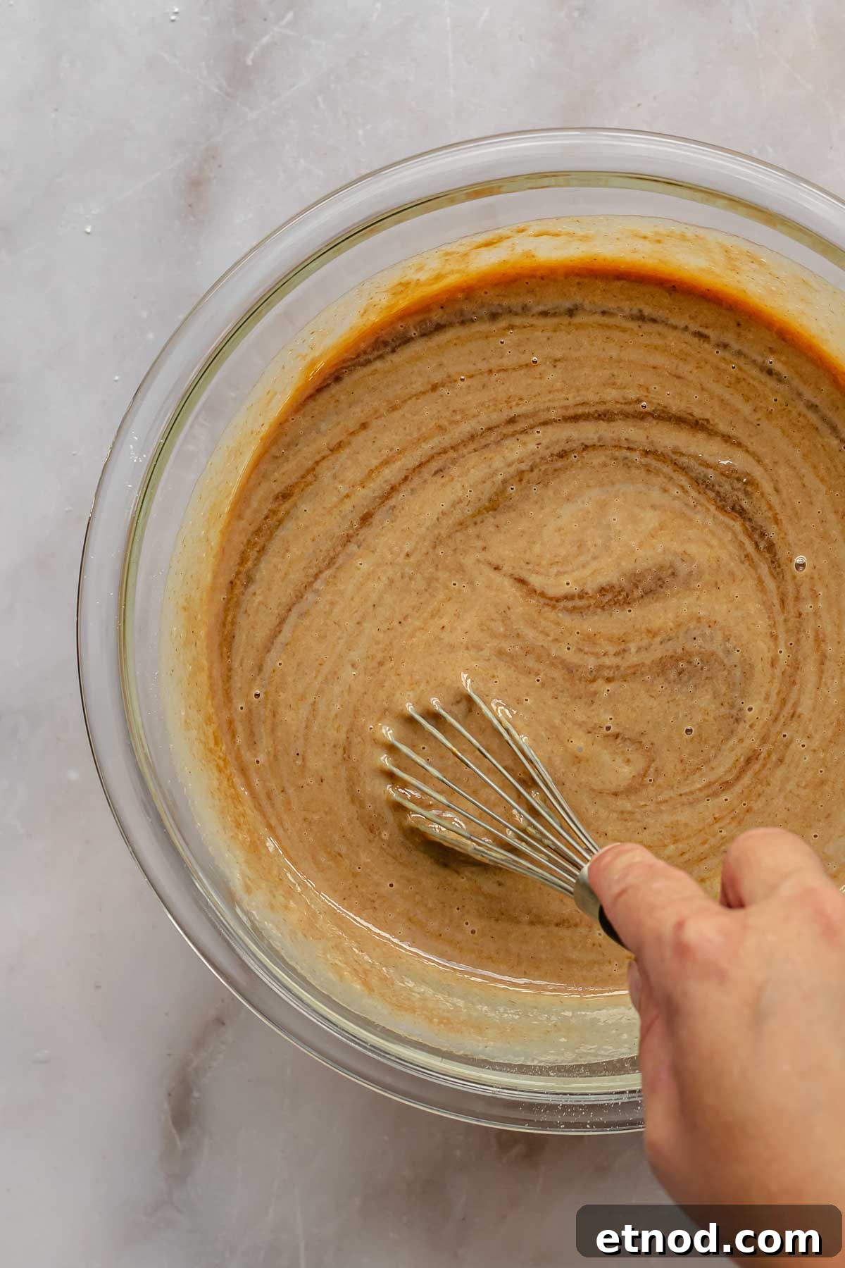 A hand whisks together ingredients for apple butter pie.