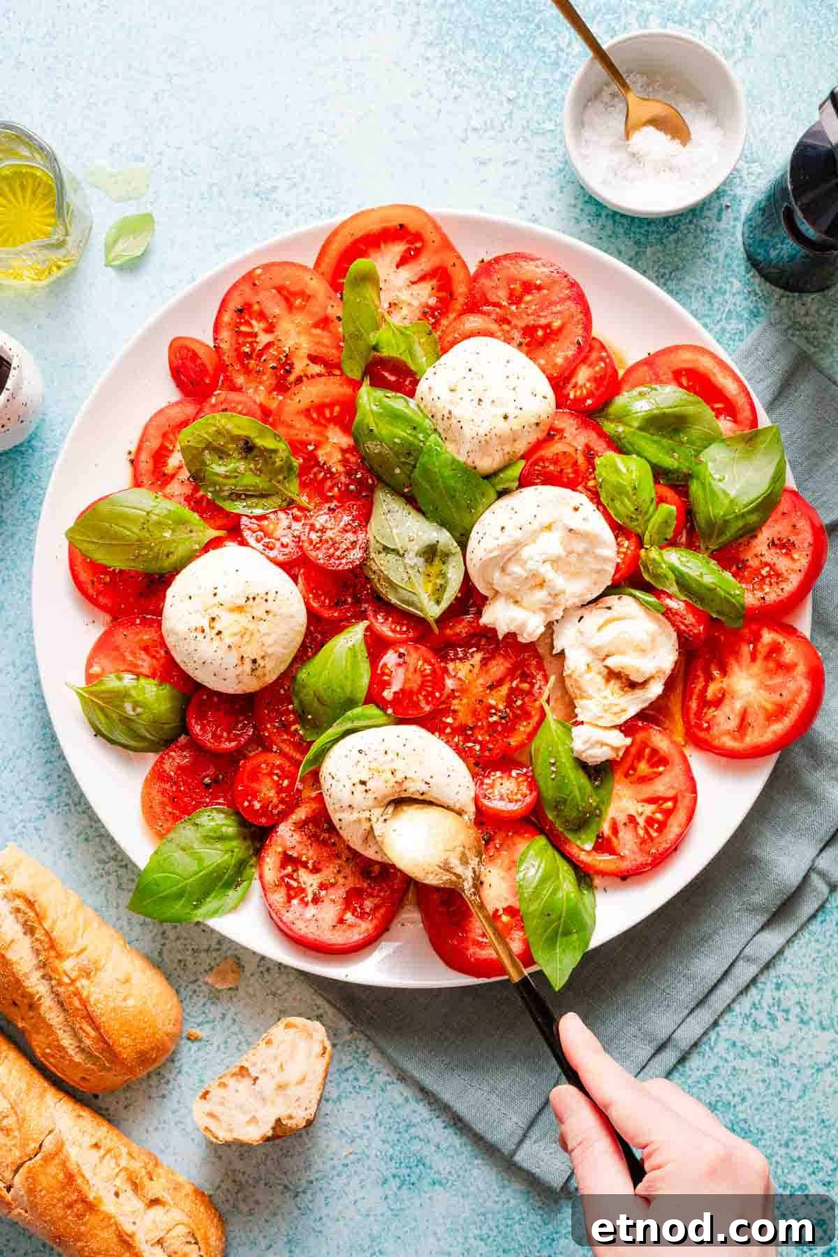 Creamy Burrata Caprese Salad with Heirloom Tomatoes 2 spoon cutting into ball of burrata on caprese salad.