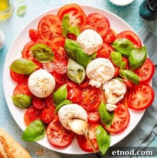 caprese salad with burrata cheese balls and bread on the side.