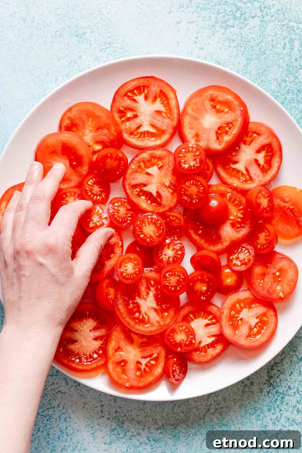 Creamy Burrata Caprese Salad with Heirloom Tomatoes 5 sliced tomatoes being placed on a white platter.