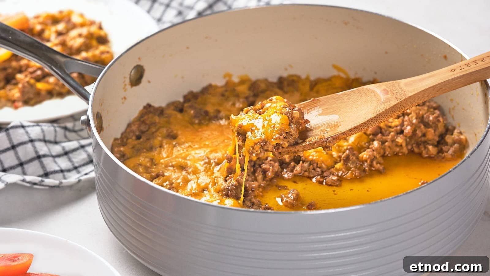 A wooden spoon scoops a portion of cooked ground meat with melted cheese from a pan.