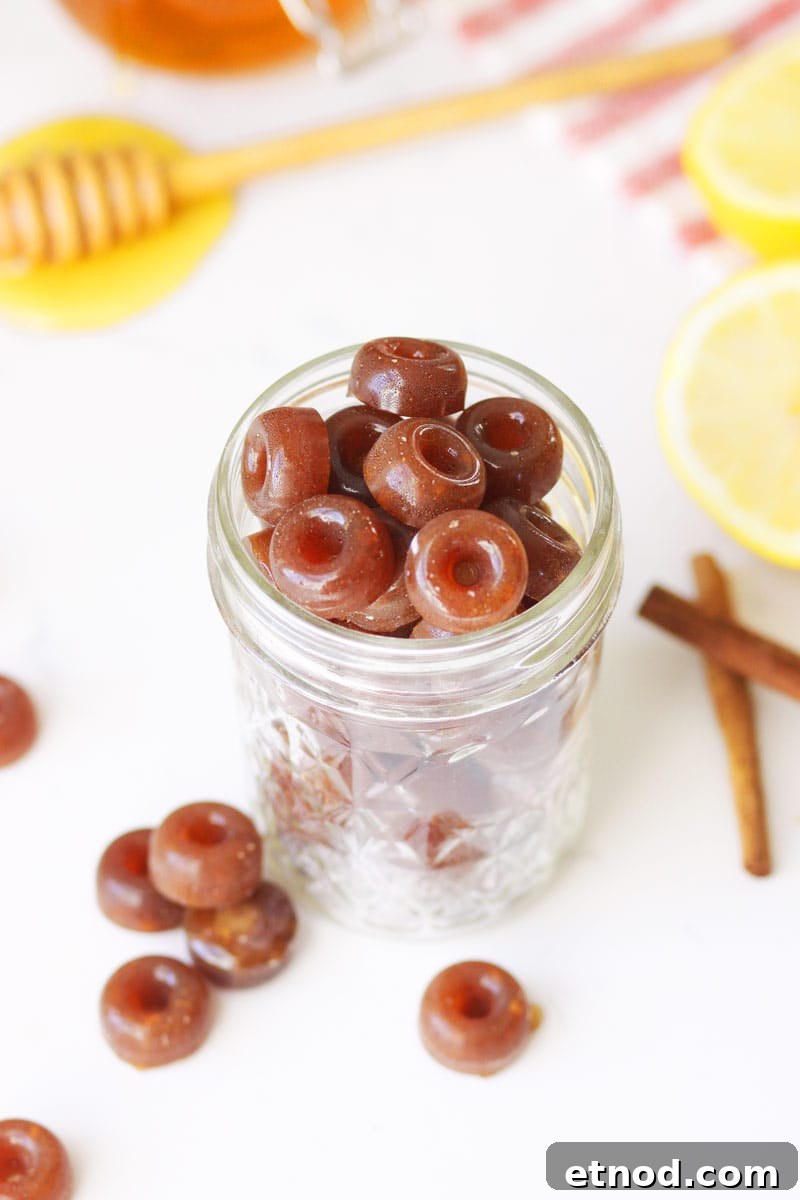 DIY Lemon, Honey & Ginger Cough Drops Recipe for Soothing Relief 2 a mason jar of homemade cough drops with ginger root, honey on a honey stir stick, lemon and cinnamon sticks on the table next to it.