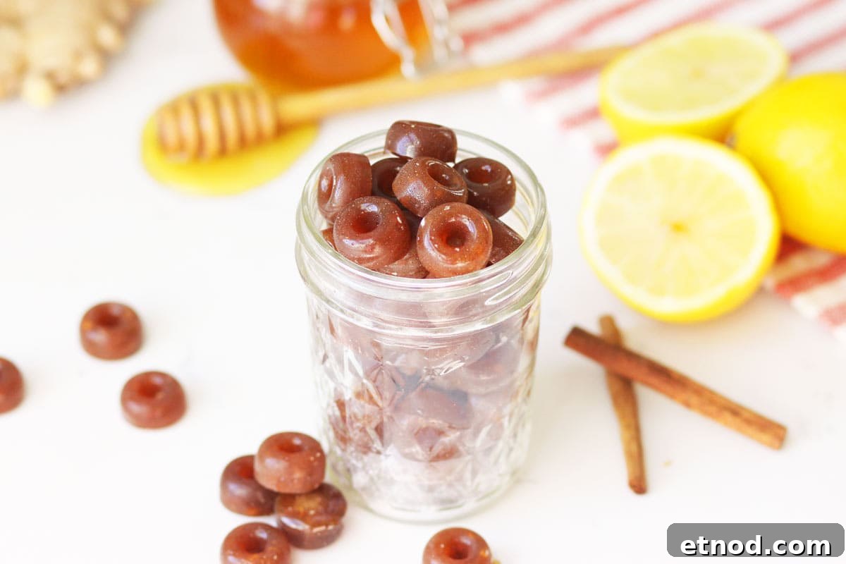 DIY Lemon, Honey & Ginger Cough Drops Recipe for Soothing Relief 3 a mason jar of homemade cough drops with ginger root, honey on a honey stir stick, lemon and cinnamon sticks on the table next to it.