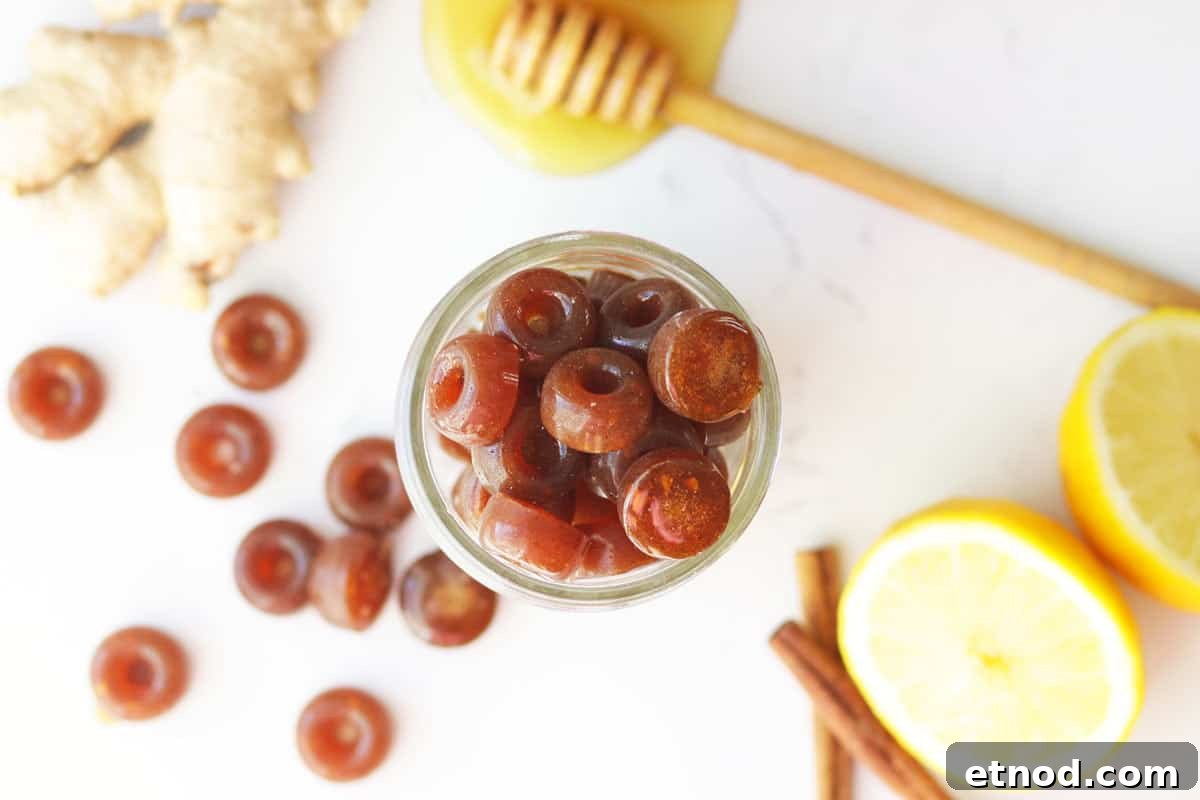 DIY Lemon, Honey & Ginger Cough Drops Recipe for Soothing Relief 5 a mason jar of homemade cough drops with ginger root, honey on a honey stir stick, lemon and cinnamon sticks on the table next to it.