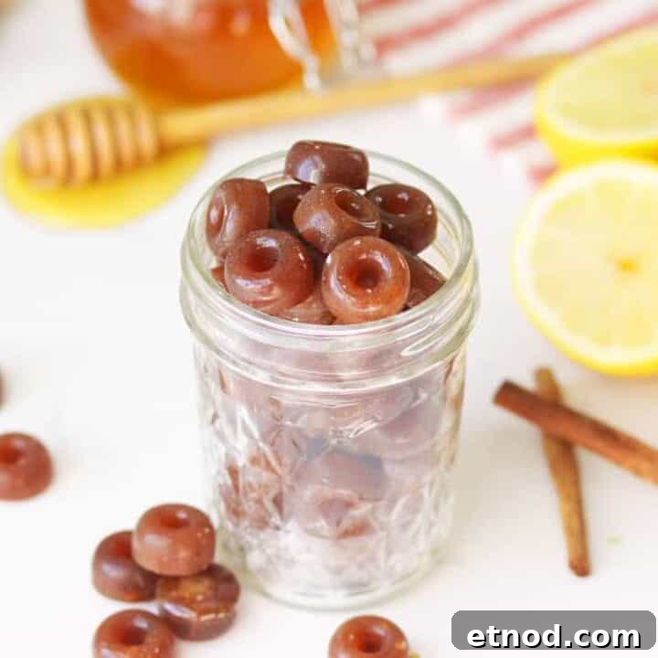 a mason jar of homemade cough drops with ginger root, honey on a honey stir stick, lemon and cinnamon sticks on the table next to it.