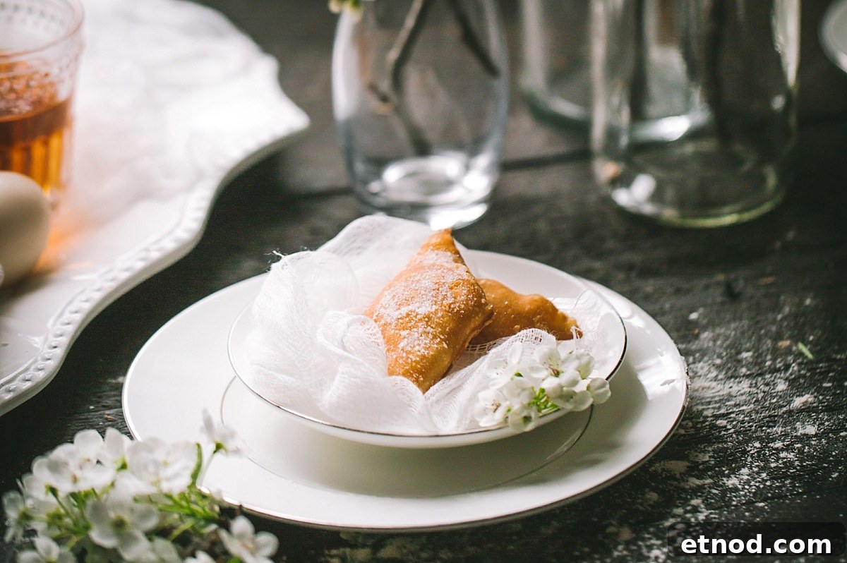 Two no yeast bugnes (French beignets) sitting on a white mesh fabric in a decorative white plate and bowl