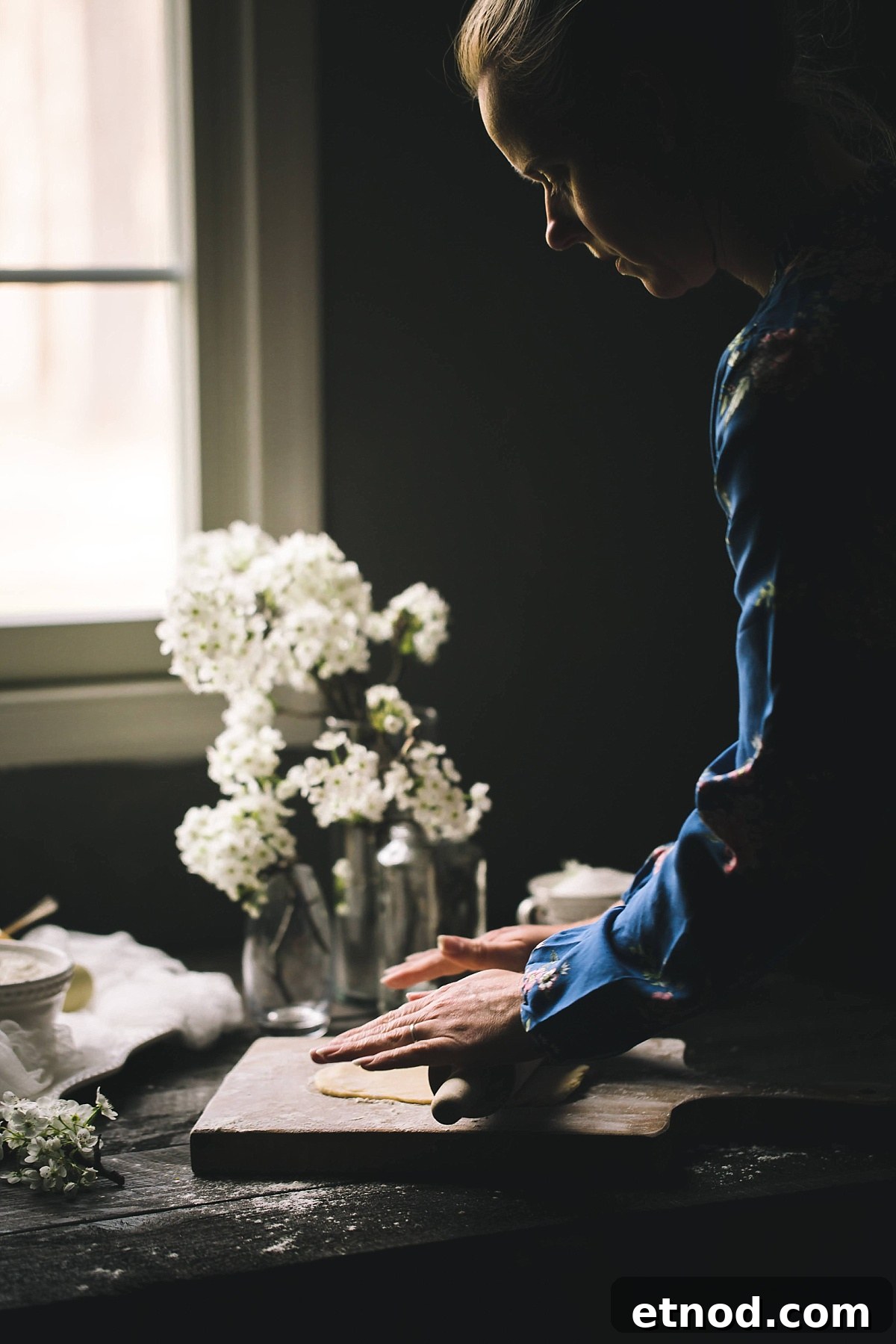 woman outlined by soft window light rolls very thin beignet dough to make bugnes lyonnaises