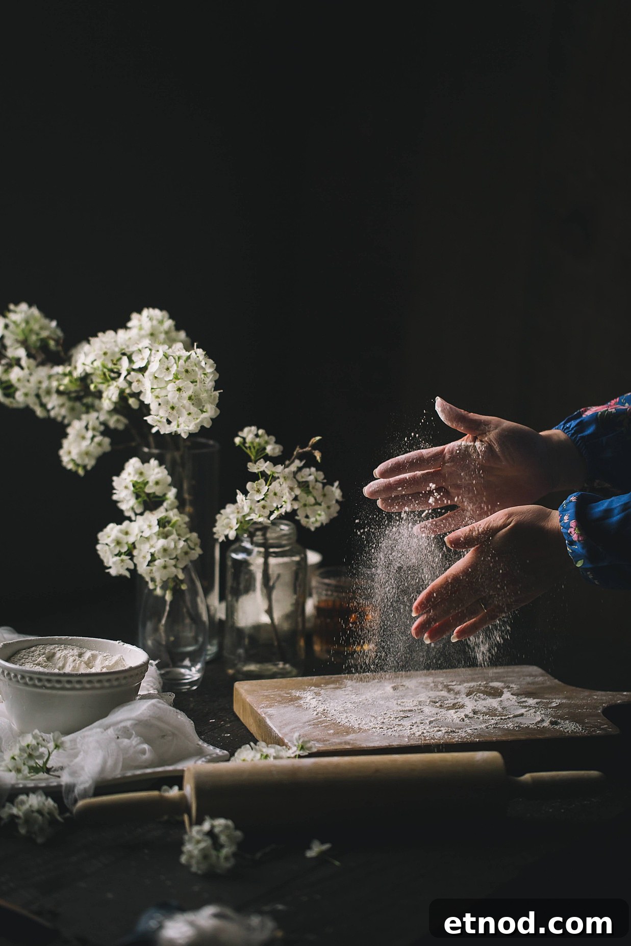 A woman clapping her floured hands while the flour goes onto a floured wooden cutting board