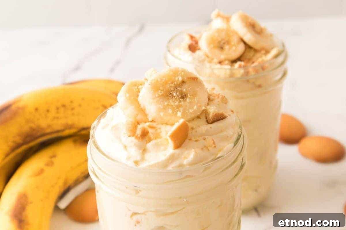 21 Quirky-Looking Desserts That Disappear First at Parties 3 Two jars of banana pudding topped with banana slices and crushed cookies are in the foreground, with bananas and vanilla wafers in the background on a white surface.