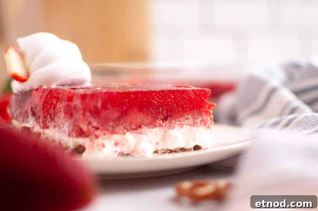 21 Quirky-Looking Desserts That Disappear First at Parties 7 A slice of strawberry pretzel salad with whipped cream on a white plate, showing layers of red gelatin, creamy filling, and pretzel crust.