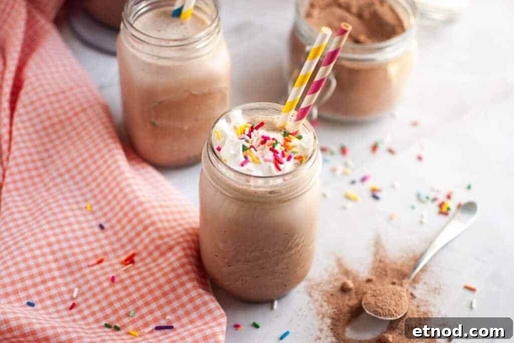 21 Quirky-Looking Desserts That Disappear First at Parties 9 A mason jar filled with a Frozen Hot Chocolate topped with whipped cream and sprinkles, two colorful straws, surrounded by jars of cocoa powder and a pink checkered cloth.