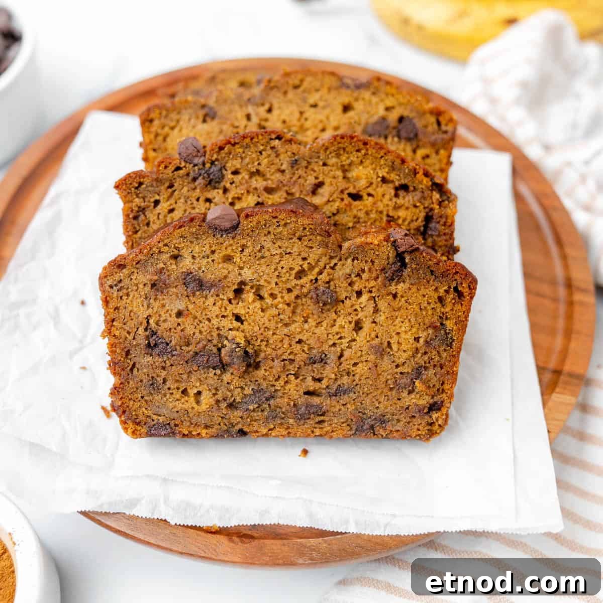 Pumpkin Banana Bread Recipe with Warm Spices and Moist Crumb 2 Three slices of chocolate chip pumpkin banana bread are arranged on a round wooden board lined with parchment paper.