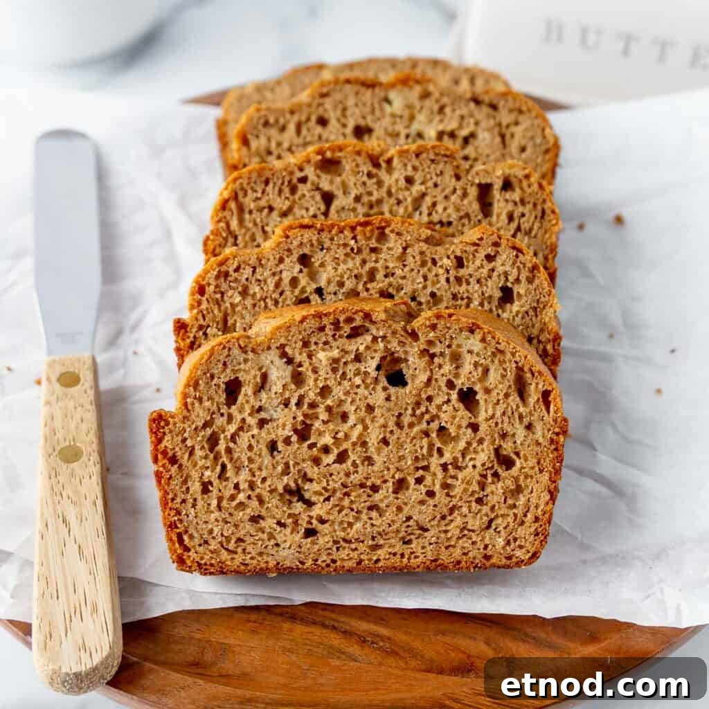 Pumpkin Banana Bread Recipe with Warm Spices and Moist Crumb 12 Four slices of banana bread are arranged on parchment paper with a butter knife on a wooden board.