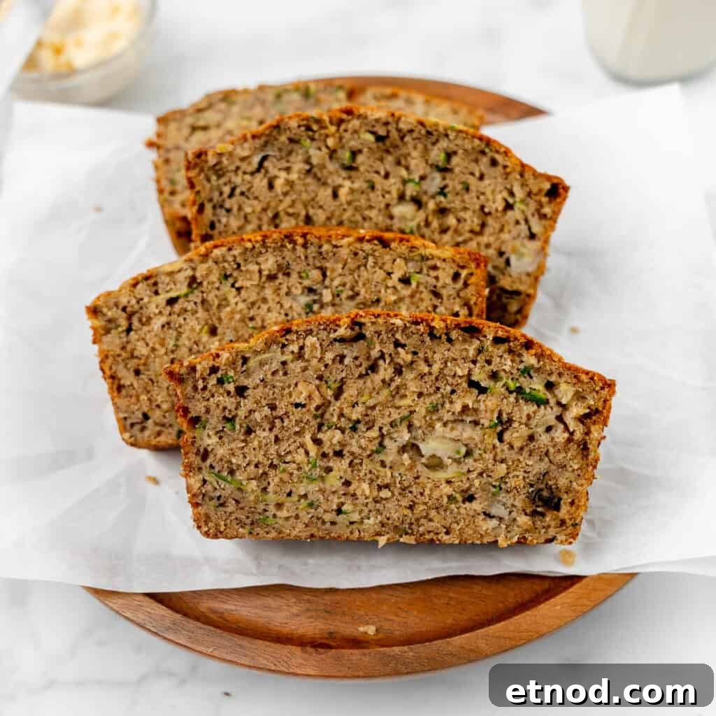 Pumpkin Banana Bread Recipe with Warm Spices and Moist Crumb 13 Three slices of zucchini bread are arranged on a wooden plate lined with parchment paper.