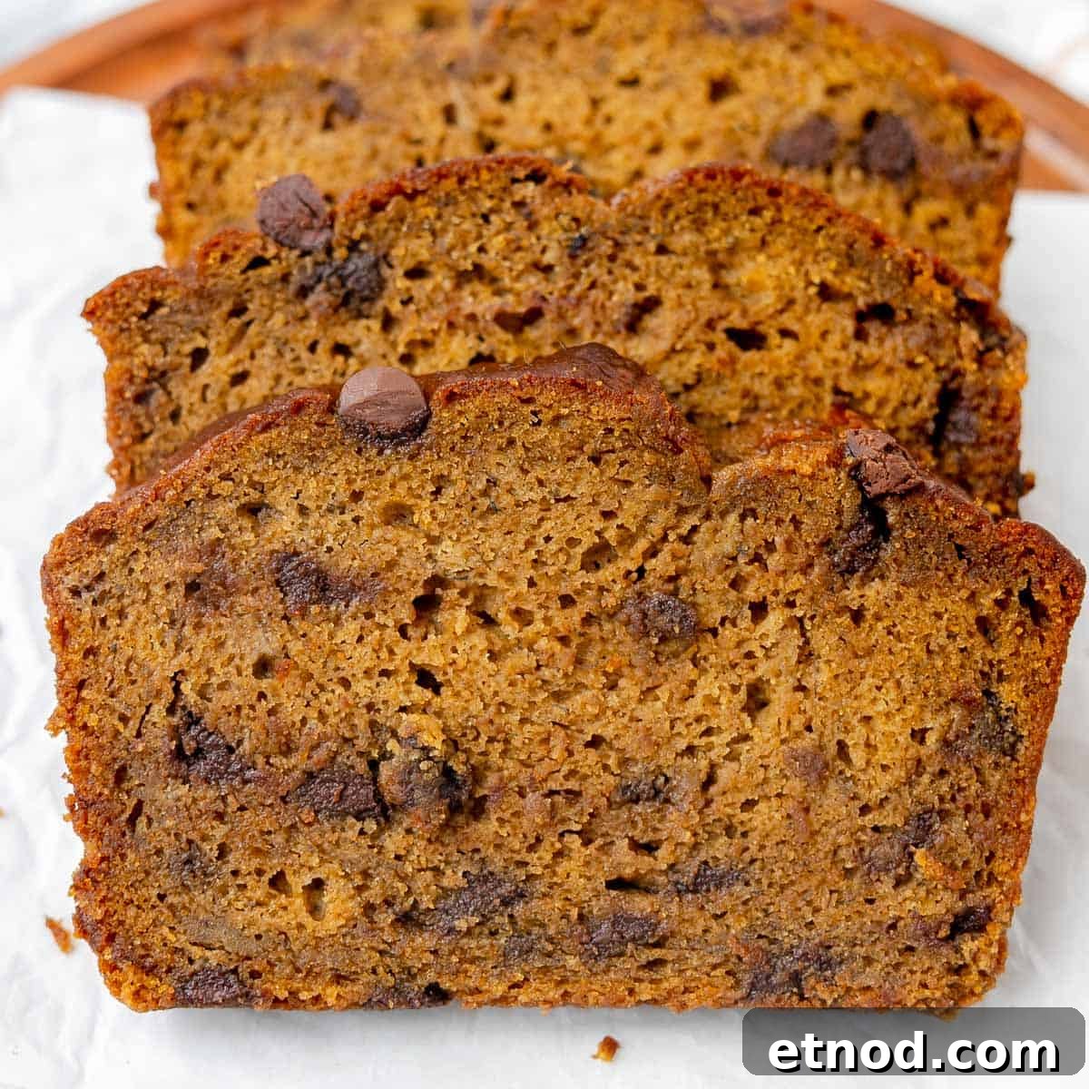 Pumpkin Banana Bread Recipe with Warm Spices and Moist Crumb 15 Three slices of chocolate chip banana bread are arranged in a row on white parchment paper.
