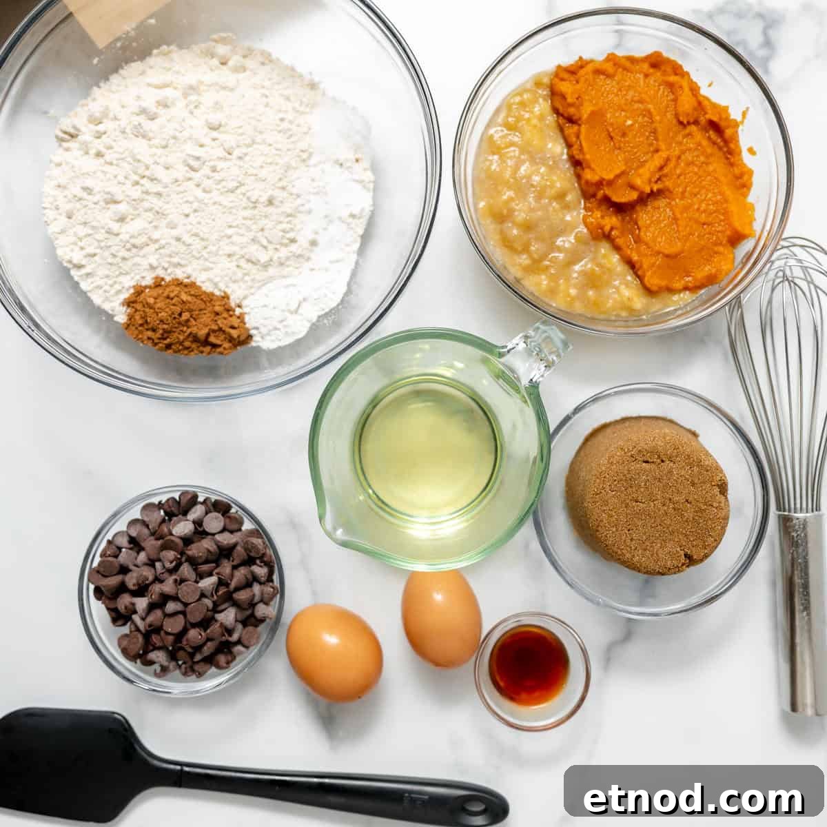 Pumpkin Banana Bread Recipe with Warm Spices and Moist Crumb 3 Bowls with flour, spices, mashed banana, pumpkin puree, chocolate chips, brown sugar, oil, two eggs, vanilla extract, a spatula, and a whisk on a white countertop.