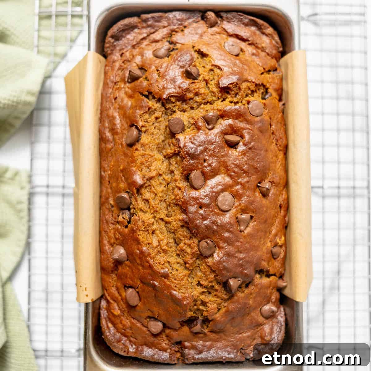 Pumpkin Banana Bread Recipe with Warm Spices and Moist Crumb 8 A loaf of chocolate chip banana bread in a metal baking pan lined with parchment paper, resting on a wire cooling rack.