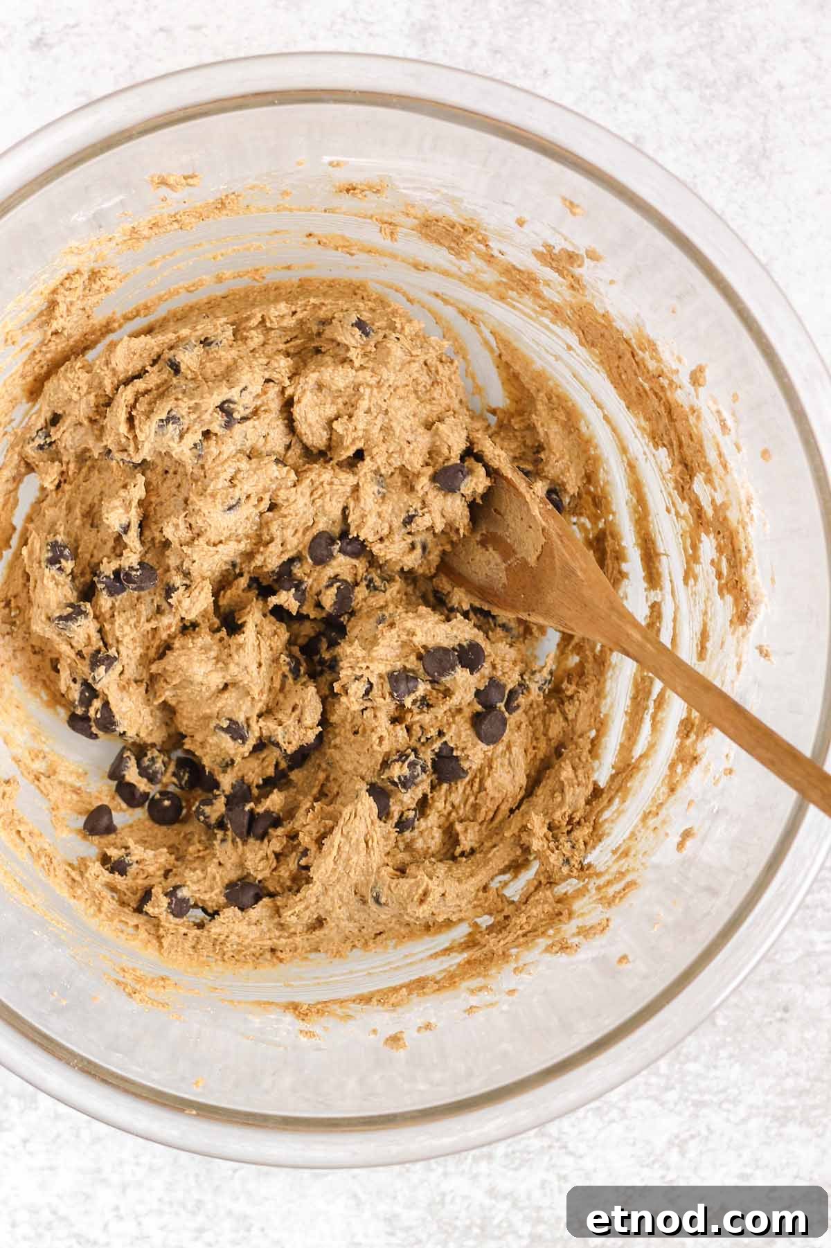 Chocolate chips folded into cookie dough with a wooden spoon.