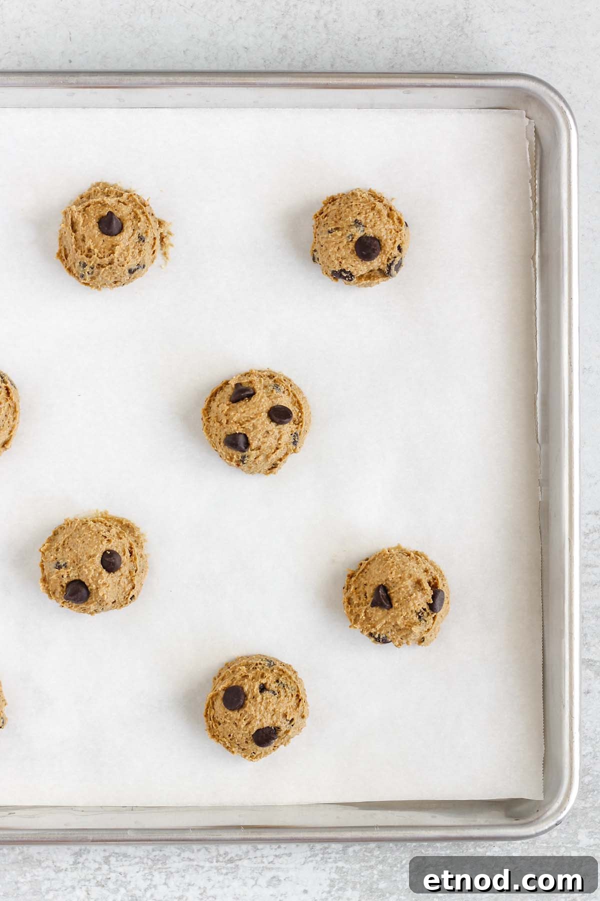 Chocolate chip cookie dough balls on a baking sheet with white parchment paper.