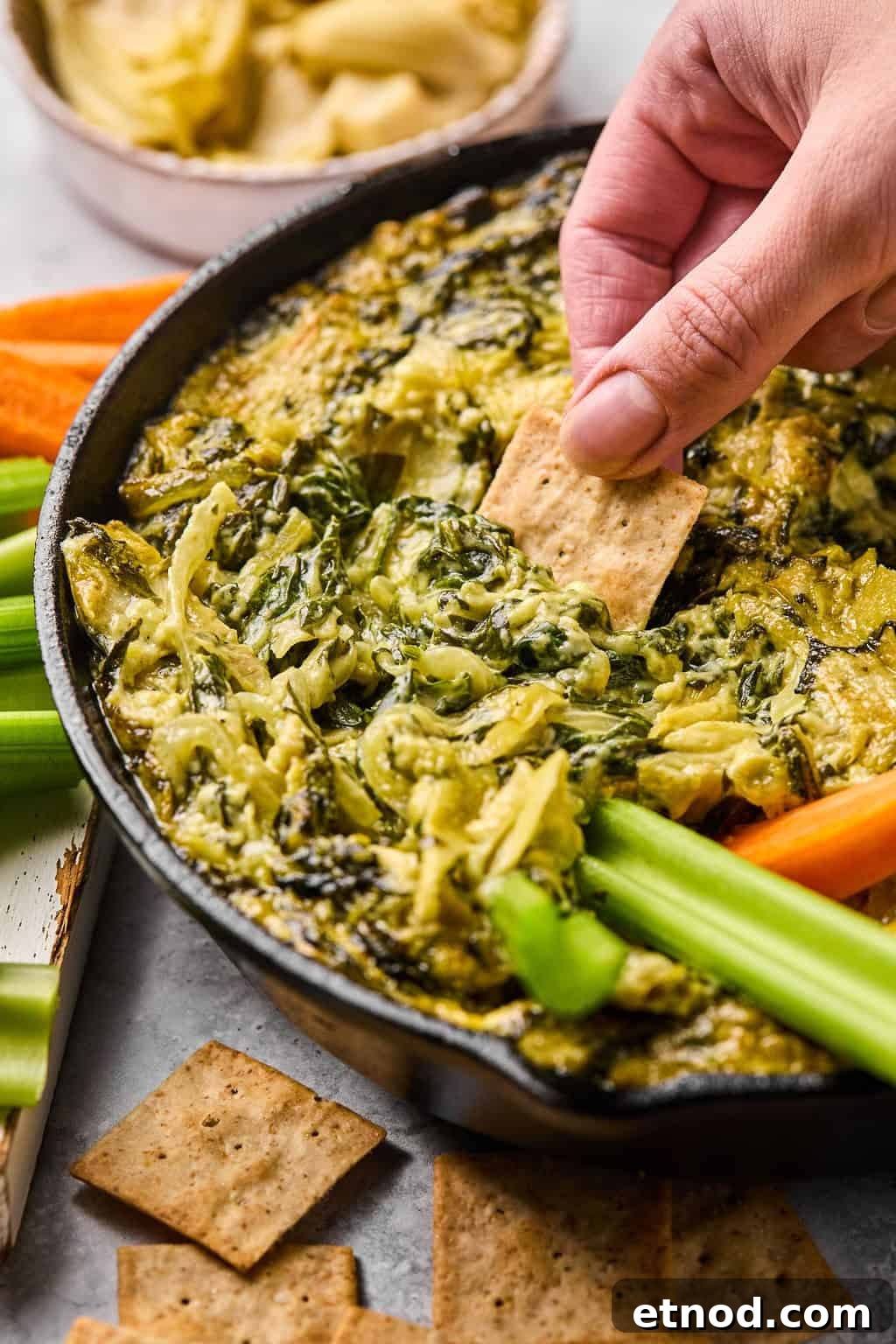 scooping dairy free spinach artichoke dip up with a gluten free cracker.