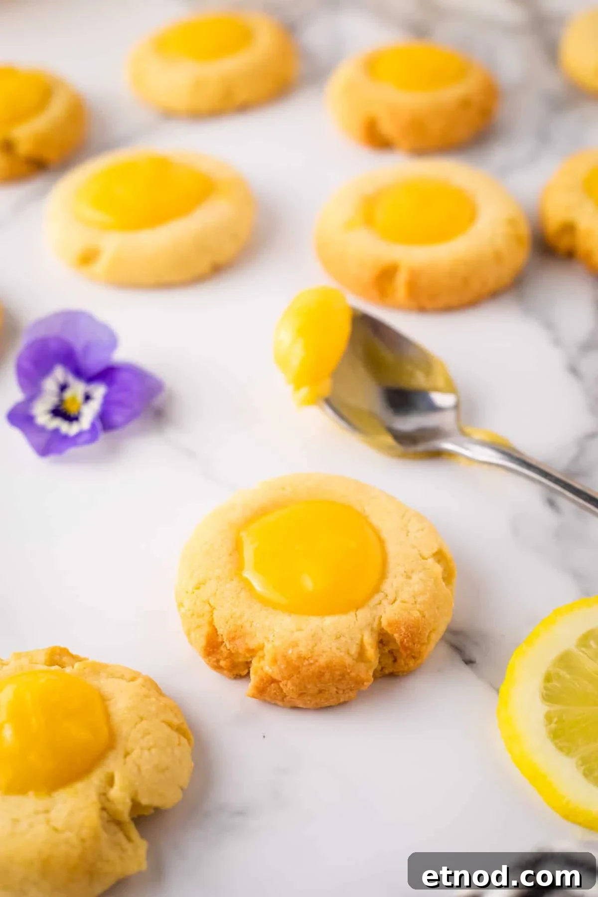 Lemon Curd Thumbprint Cookies — Zesty Jam-Filled Shortbread 2 Close up of lemon curd cookie with spoonful of lemon curd and lavender flower in background.