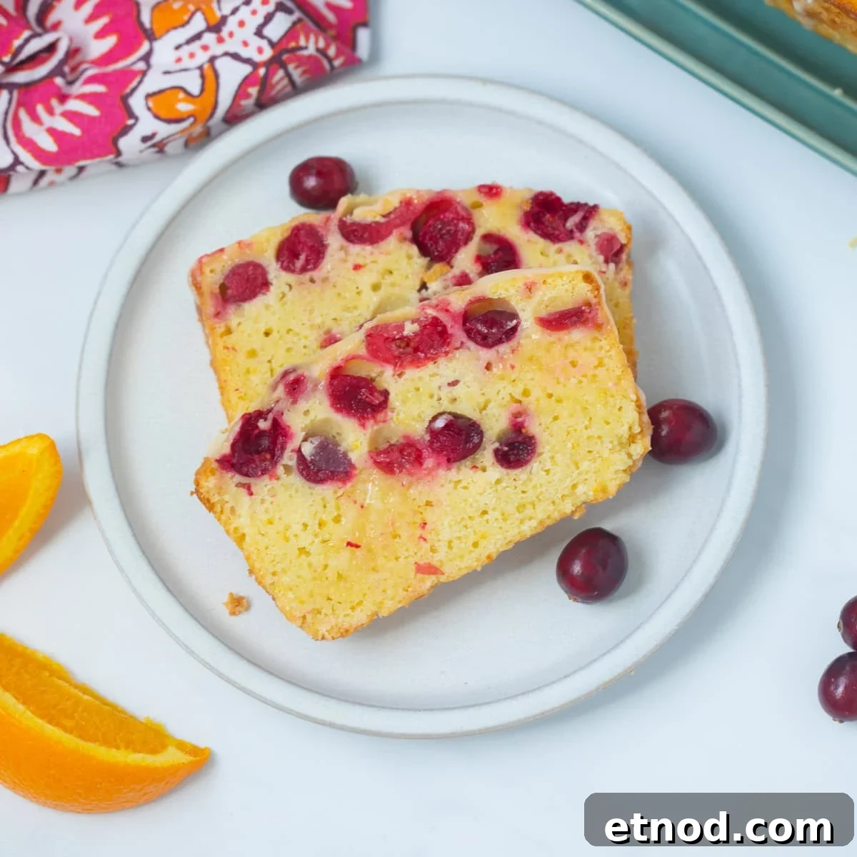 Cranberry Orange Bread Two slices of cranberry orange bread on plate next to fresh cranberries and orange slices.