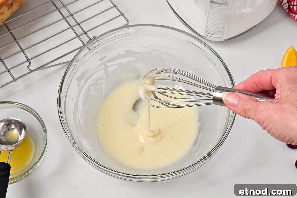 Cranberry Orange Bread recipe Wire whisk showing orange glaze dripping into mixing bowl with sugar and orange juice whisked together.