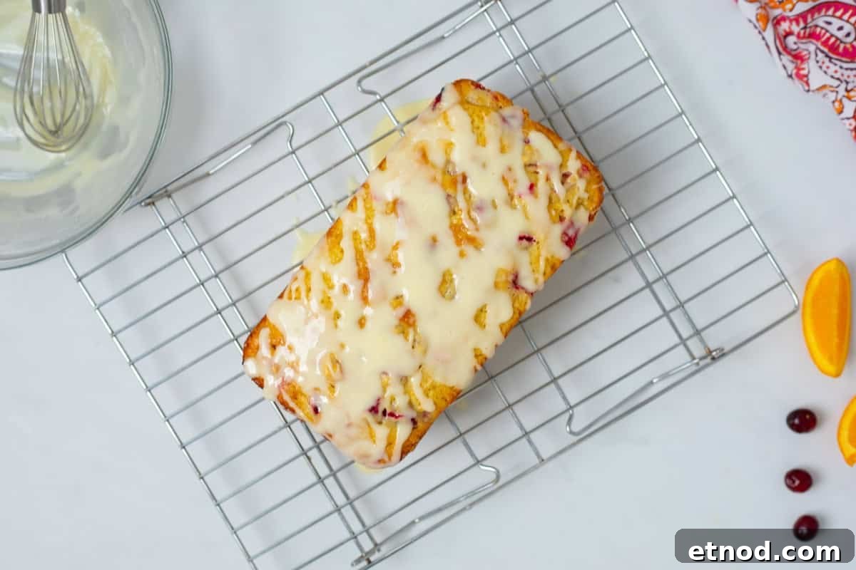 Glazed Cranberry Orange Bread Cranberry Orange Loaf on wire cooling rack after being drizzled with simple orange glaze.